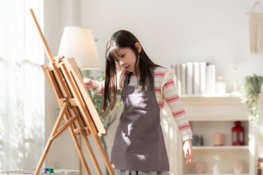 Evde bir oturma odasında odaklanmış ve yaratıcılıkla resim yapan küçük bir kız.