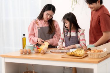 Kızlarının mutfakta hamuru sarmasına yardım eden bir aile, eğlenceli bir pişirme anının tadını çıkarıyor.