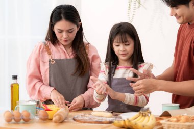 Kızlarının mutfakta hamuru sarmasına yardım eden bir aile, eğlenceli bir pişirme anının tadını çıkarıyor.