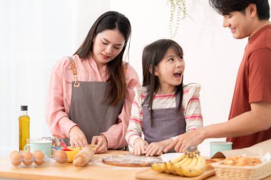 Kızlarının mutfakta hamuru sarmasına yardım eden bir aile, eğlenceli bir pişirme anının tadını çıkarıyor.