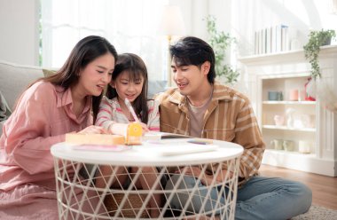 Parlak bir oturma odasında, küçük bir masada kızlarına sanat ve öğrenim faaliyetlerinde yardım eden bir aile.