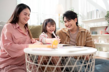 Parlak bir oturma odasında, küçük bir masada kızlarına sanat ve öğrenim faaliyetlerinde yardım eden bir aile.