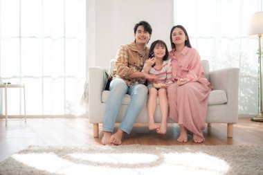 Bir aile birlikte kanepede oturuyor, televizyon izliyor ve parlak bir oturma odasında patlamış mısırın tadını çıkarıyor.