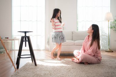 Bir anne yerde diz çöker ve kızına sıcak bir kucaklama yapar. Parlak, rahat bir oturma odasında, neşe ve güçlü aile bağlarını ifade eder.