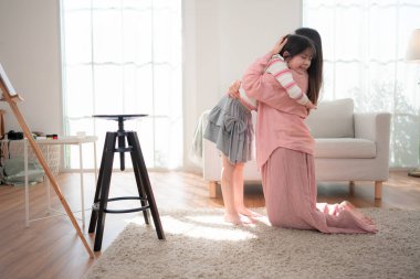 Bir anne yerde diz çöker ve kızına sıcak bir kucaklama yapar. Parlak, rahat bir oturma odasında, neşe ve güçlü aile bağlarını ifade eder.