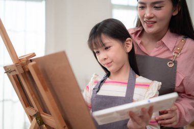 Bir anne, resim yaparken kızına rehberlik eder. Parlak ve rahat bir oturma odasında yaratıcı bir öğrenme anını paylaşır.