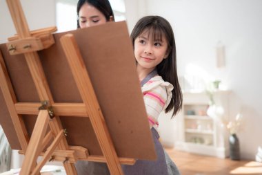 Bir anne, resim yaparken kızına rehberlik eder. Parlak ve rahat bir oturma odasında yaratıcı bir öğrenme anını paylaşır.