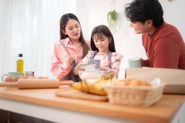 Kızlarının mutfakta hamuru sarmasına yardım eden bir aile, eğlenceli bir pişirme anının tadını çıkarıyor.