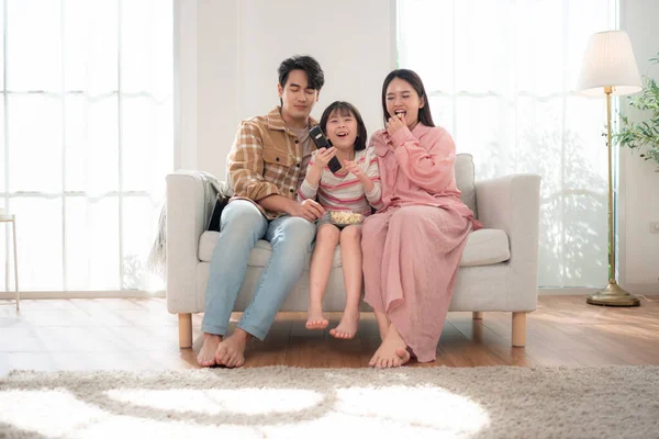 Bir aile birlikte kanepede oturuyor, televizyon izliyor ve parlak bir oturma odasında patlamış mısırın tadını çıkarıyor.