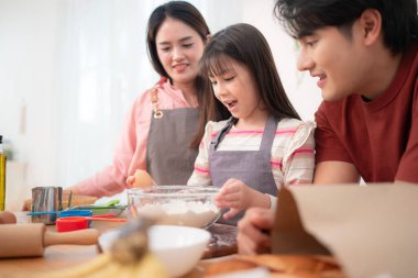 Kızlarının mutfakta hamuru sarmasına yardım eden bir aile, eğlenceli bir pişirme anının tadını çıkarıyor.