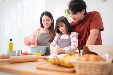 Kızlarının mutfakta hamuru sarmasına yardım eden bir aile, eğlenceli bir pişirme anının tadını çıkarıyor.