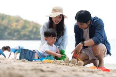 Tatilde, plajda birlikte oynayan genç bir aile, güneşli bir sahil tatili sırasında çocuklarının kumdan kale yapmalarına yardım eden aileler.