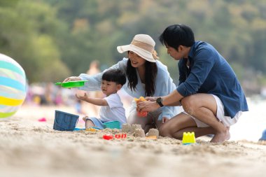 Tatilde, plajda birlikte oynayan genç bir aile, güneşli bir sahil tatili sırasında çocuklarının kumdan kale yapmalarına yardım eden aileler.