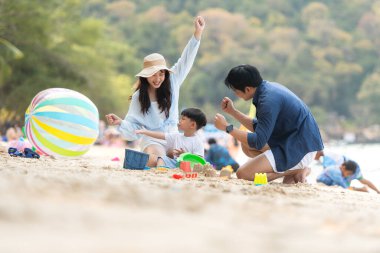 Tatilde, plajda birlikte oynayan genç bir aile, güneşli bir sahil tatili sırasında çocuklarının kumdan kale yapmalarına yardım eden aileler.