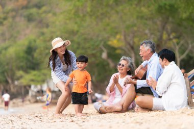 Yaşlı adam gitar çalarken, kum plajında birlikte oturan çok nesilli bir aile ve büyükanne ve çocuk gündüz vakti birlikte vakit geçiriyorlar.