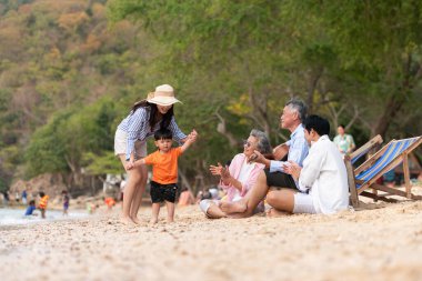 Yaşlı adam gitar çalarken, kum plajında birlikte oturan çok nesilli bir aile ve büyükanne ve çocuk gündüz vakti birlikte vakit geçiriyorlar.