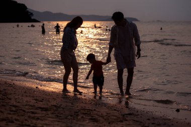 Tatilde ebeveynler, gün batımında sahilde sığ deniz suyunda yürürken küçük çocuklarıyla birlikte.