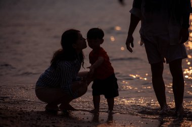Tatilde ebeveynler, gün batımında sahilde sığ deniz suyunda yürürken küçük çocuklarıyla birlikte.