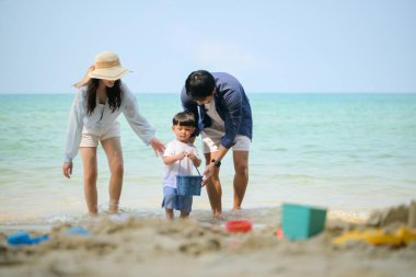 Tatilde ebeveynler, gün içinde deniz kenarındaki kumsalda birlikte oyuncak oynarken küçük çocuklarıyla birlikte duruyorlar.