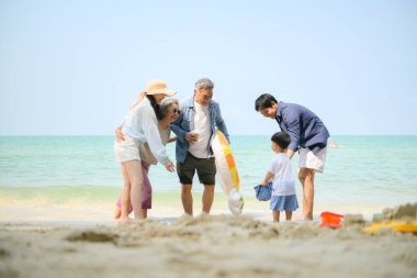 Genişletilmiş aile gündüz vakti deniz kenarında kumlu kumsalda ayakta durup şişme halkalarla oynuyor.