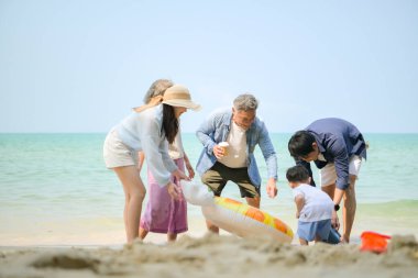 Genişletilmiş aile gündüz vakti deniz kenarında kumlu kumsalda ayakta durup şişme halkalarla oynuyor.