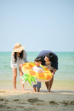 Tatilde ebeveynler, gün içinde deniz kenarındaki kumsalda küçük çocuklarıyla birlikte şişme bir halka yakalarken...