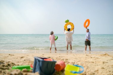 Tatilde, aile üyeleri gün içinde deniz kenarında dururken havaya şişirilebilir yüzükler fırlatıp zıplıyorlar.