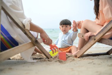 Tatilde, ebeveynler plaj sandalyelerinde oturup, gün boyunca çocuklarının kumsalda kum oyuncaklarıyla oynamasını seyrederler.
