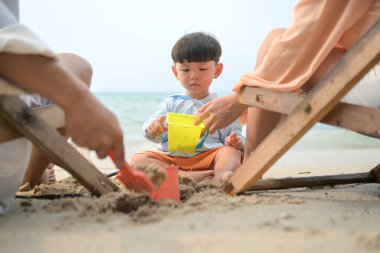 Tatilde, ebeveynler plaj sandalyelerinde oturup, gün boyunca çocuklarının kumsalda kum oyuncaklarıyla oynamasını seyrederler.
