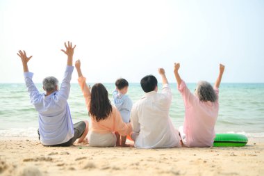 Tatilde, uzanmış aile kumsalda oturup birlikte el kaldırırken gün içinde sahile bakıyor.