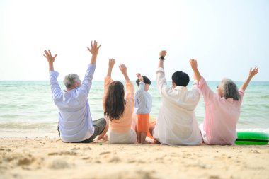 Tatilde, uzanmış aile kumsalda oturup birlikte el kaldırırken gün içinde sahile bakıyor.