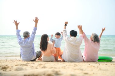 Tatilde, uzanmış aile kumsalda oturup birlikte el kaldırırken gün içinde sahile bakıyor.