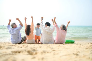 Tatilde, uzanmış aile kumsalda oturup birlikte el kaldırırken gün içinde sahile bakıyor.