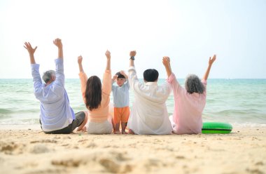 Tatilde, uzanmış aile kumsalda oturup birlikte el kaldırırken gün içinde sahile bakıyor.