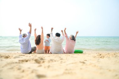 Tatilde, uzanmış aile kumsalda oturup birlikte el kaldırırken gün içinde sahile bakıyor.