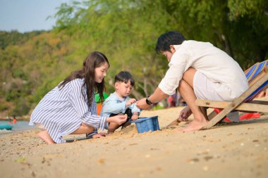 Tatilde, ebeveynler plaj sandalyelerinde oturup, gün boyunca çocuklarının kumsalda kum oyuncaklarıyla oynamasını seyrederler.