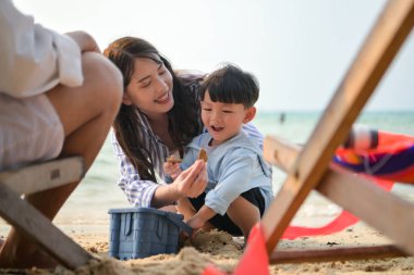 Tatilde, ebeveynler plaj sandalyelerinde oturup, gün boyunca çocuklarının kumsalda kum oyuncaklarıyla oynamasını seyrederler.