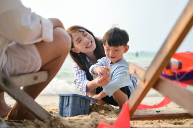 Tatilde, ebeveynler plaj sandalyelerinde oturup, gün boyunca çocuklarının kumsalda kum oyuncaklarıyla oynamasını seyrederler.