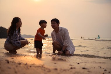 Ebeveynler gün batımında sahilde sığ deniz suyunda yürürken küçük çocuklarıyla el ele tutuşuyorlar.
