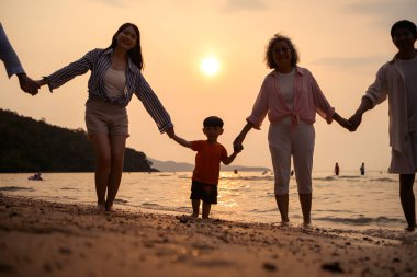 Ebeveynler gün batımında sahilde sığ deniz suyunda yürürken küçük çocuklarıyla el ele tutuşuyorlar.