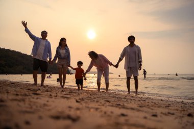 Ebeveynler gün batımında sahilde sığ deniz suyunda yürürken küçük çocuklarıyla el ele tutuşuyorlar.