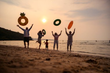 Mutlu çoklu nesil aile gün batımının tadını çıkarıyor. Renkli şişme yüzme yüzükleri atıyor. Deniz kenarında özgürlük, neşe ve yaz yaşam tarzını ifade ediyor.