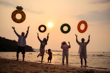 Mutlu çoklu nesil aile gün batımının tadını çıkarıyor. Renkli şişme yüzme yüzükleri atıyor. Deniz kenarında özgürlük, neşe ve yaz yaşam tarzını ifade ediyor.