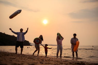 Mutlu çoklu nesil aile gün batımının tadını çıkarıyor. Renkli şişme yüzme yüzükleri atıyor. Deniz kenarında özgürlük, neşe ve yaz yaşam tarzını ifade ediyor.