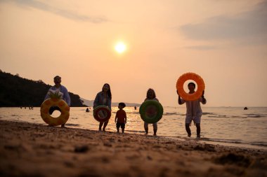 Mutlu çoklu nesil aile gün batımının tadını çıkarıyor. Renkli şişme yüzme yüzükleri atıyor. Deniz kenarında özgürlük, neşe ve yaz yaşam tarzını ifade ediyor.