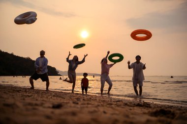 Mutlu çoklu nesil aile gün batımının tadını çıkarıyor. Renkli şişme yüzme yüzükleri atıyor. Deniz kenarında özgürlük, neşe ve yaz yaşam tarzını ifade ediyor.