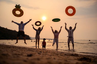 Mutlu çoklu nesil aile gün batımının tadını çıkarıyor. Renkli şişme yüzme yüzükleri atıyor. Deniz kenarında özgürlük, neşe ve yaz yaşam tarzını ifade ediyor.