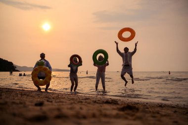 Gün batımında aile zıplıyor ve sahilde oynuyor, siluetler ıslak kumu yansıtıyordu, yaz yolculuğunu, özgürlüğü ve birlikte neşeli deniz hayatı kutluyorlardı.