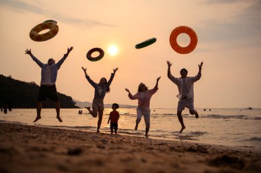 Mutlu çoklu nesil aile gün batımının tadını çıkarıyor. Renkli şişme yüzme yüzükleri atıyor. Deniz kenarında özgürlük, neşe ve yaz yaşam tarzını ifade ediyor.