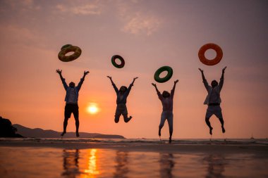 Gün batımında aile zıplıyor ve sahilde oynuyor, siluetler ıslak kumu yansıtıyordu, yaz yolculuğunu, özgürlüğü ve birlikte neşeli deniz hayatı kutluyorlardı.